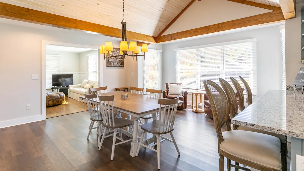 A spacious dining area featuring a large dining table under a chandelier, expansive windows, and a view toward the kitchen bar. The setup is ideal for family meals, friendly gatherings, and special celebrations, with ample natural light creating a warm, welcoming mood.