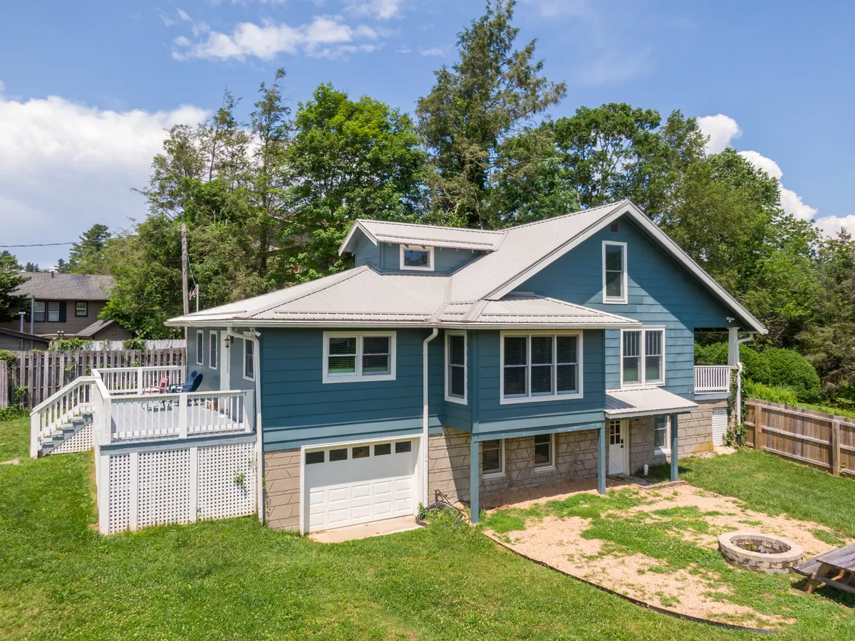 This image captures the blue exterior of the house, a spacious deck area, a cozy fire pit, and a lush green lawn. The setting is perfect for outdoor gatherings or unwinding after exploring town, with ample space for both quiet relaxation and group activities.