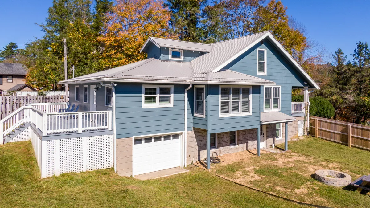 A cheerful view of the home’s blue exterior, large deck, landscaped grounds, and a fire pit area. The setting is lively and inviting, hinting at easy transitions from home to outdoor activities and nearby adventures.