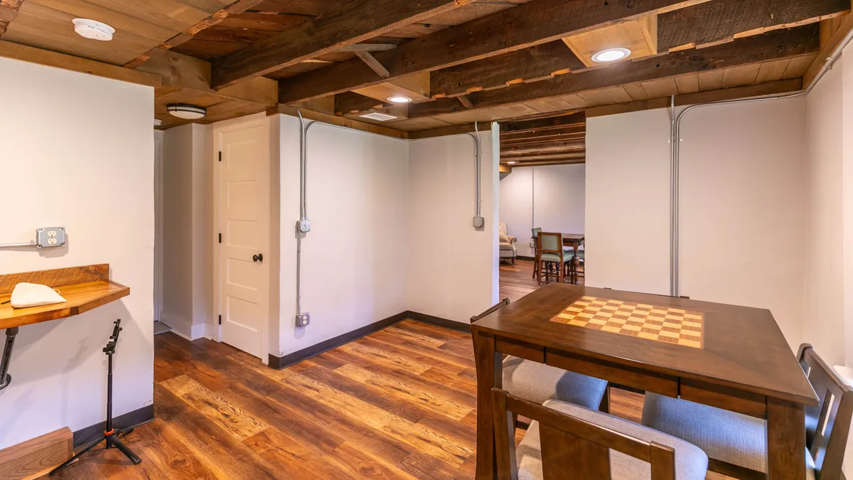 This image features a cozy interior space with a chess table, wooden flooring, and exposed ceiling beams. The intimate setting hints at a retreat perfect for board games, quiet conversation, or relaxed activities, making it well-suited to illustrate the hidden den's vintage-inspired charm.