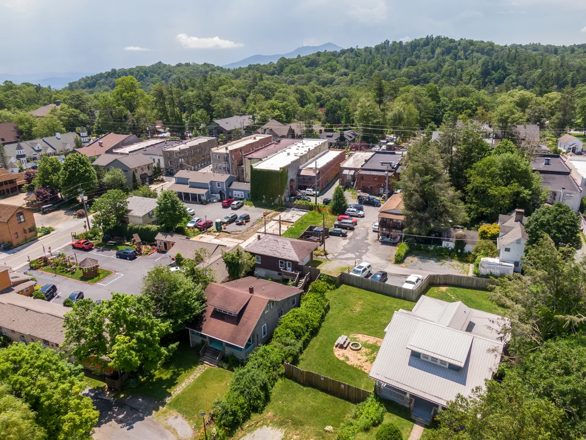 This view showcases the broader Blowing Rock neighborhood, revealing houses, commercial buildings, and parking lots bordered by a tree line. The perspective alludes to the connection between the home and the walkable community, as well as the outdoor events and friendly atmosphere described.
