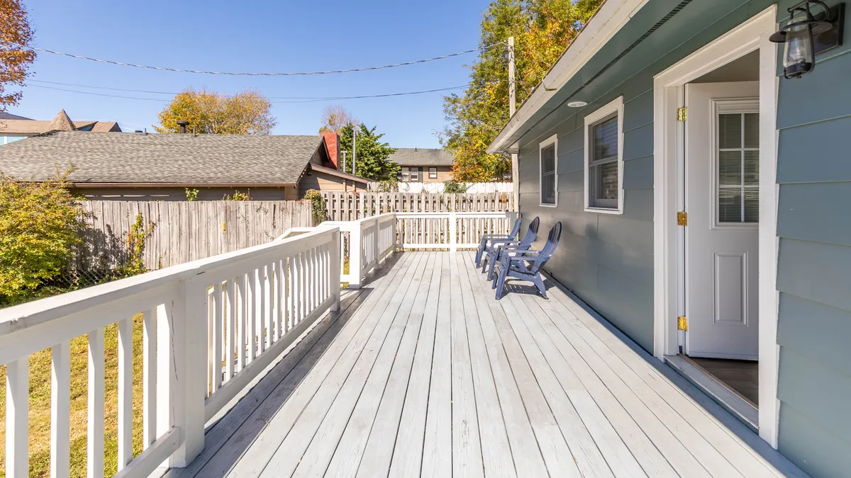 The image displays a tranquil deck with adirondack chairs and the exterior of the house, inviting guests to relax after a day exploring downtown. The setting hints at both morning and evening enjoyment, blending home comfort with outdoor access.