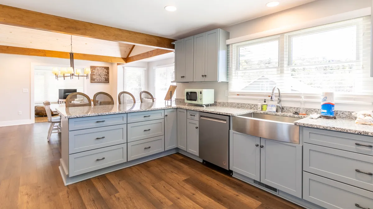 A warm, contemporary kitchen with a prominent kitchen island, granite countertop, stainless steel appliances, and exposed wooden beams. The space feels both inviting and modern, emphasizing togetherness through its layout and design.