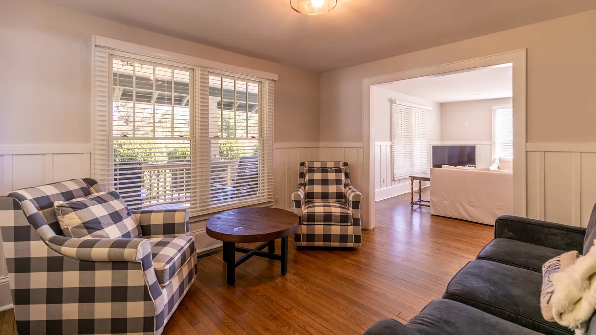 A cozy nook with plaid armchairs, a round wooden table, and expansive windows framing the morning light. The space is ideal for reading, socializing, or enjoying a warm beverage as sunlight pours in, enhancing the tranquil ambiance described in the section.