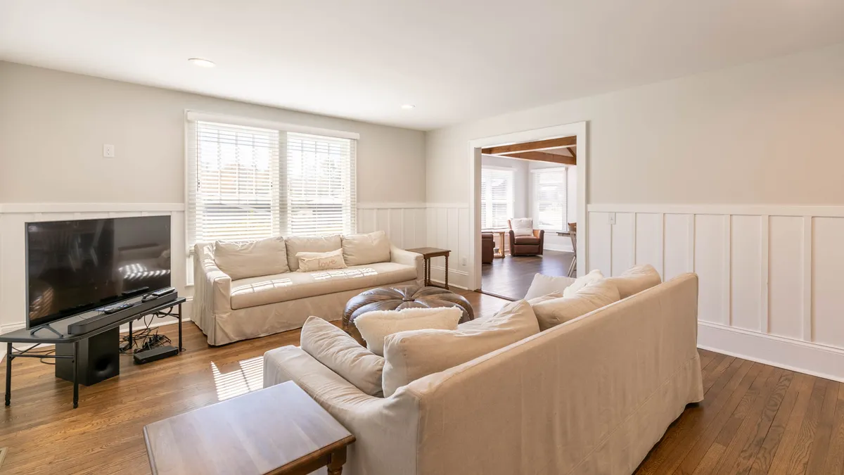 This light-filled sitting room includes comfortable seating arranged for conversation, large windows that invite in natural sunlight, and a television for entertainment. The space fosters a welcoming and social atmosphere, perfect for relaxing after a day of exploring or enjoying a casual movie night with loved ones.