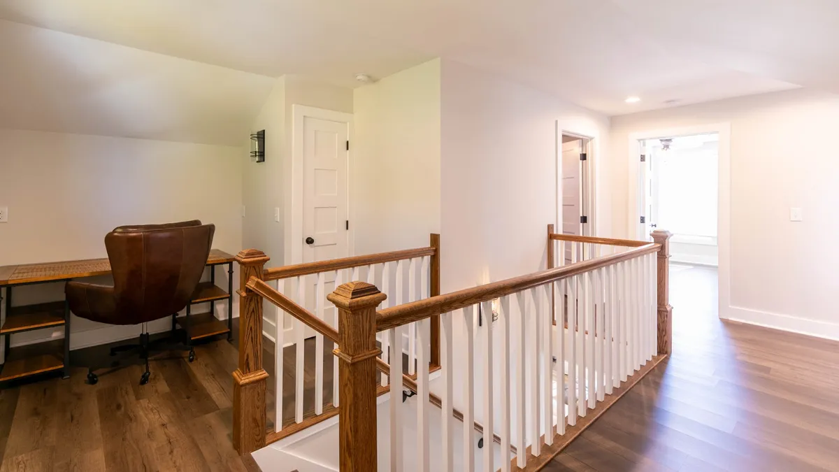A functional desk nook with a wooden railing, a sleek desk and chair, and a window letting in natural daylight. The space is both productive and cozy, offering a quiet corner for work or focused tasks within the home.