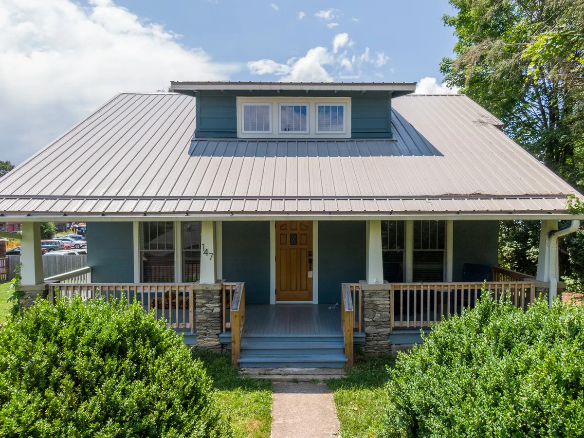 The image features the charming exterior of a beautifully updated Craftsman bungalow, highlighting an inviting front porch framed by double doors and stone accents, surrounded by lush, landscaped bushes. The scene evokes warmth and relaxation, perfect for gatherings or quiet mornings in the sun.